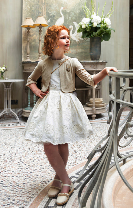 Ecru jurk in broderie anglaise en een goudkleurige cardigan