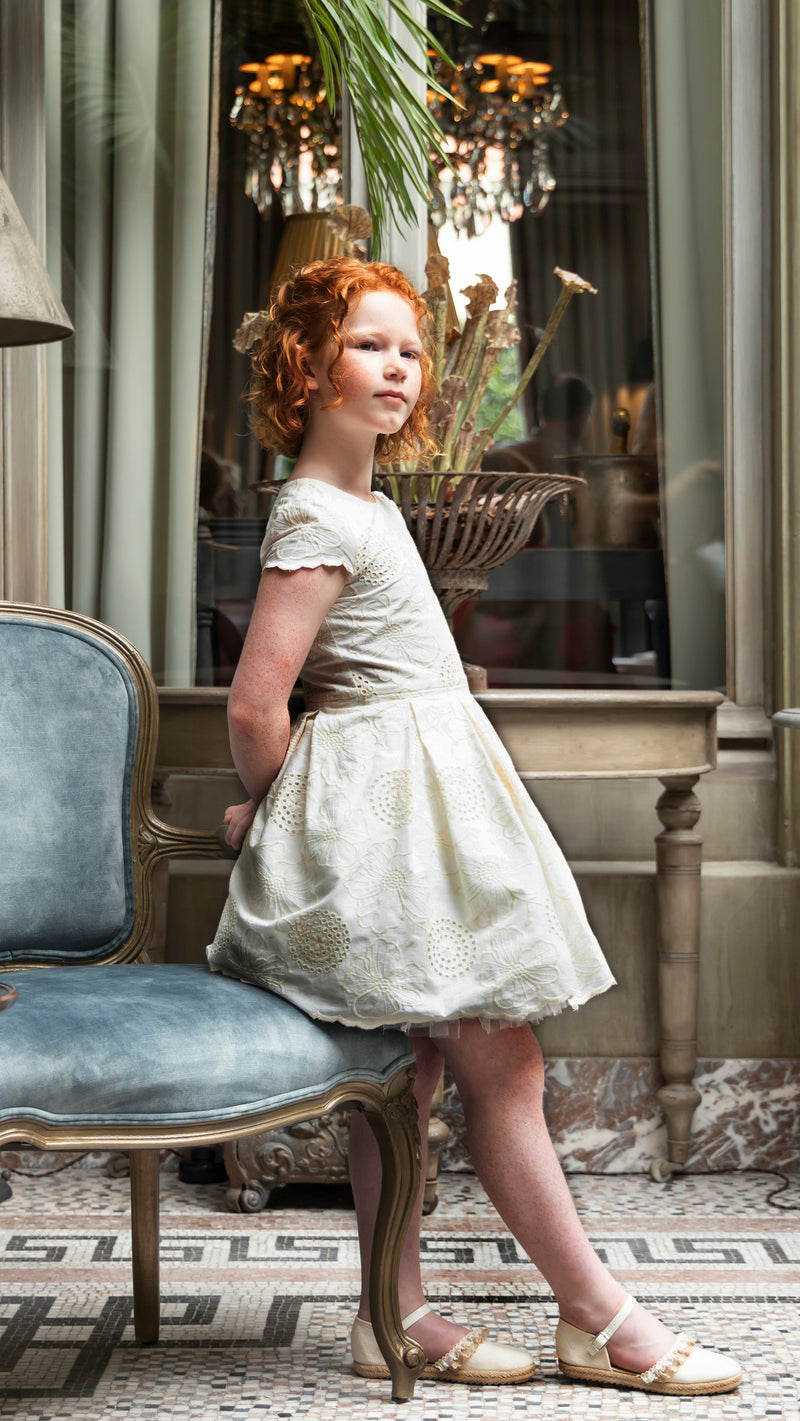 Ecru jurk in broderie anglaise en een goudkleurige cardigan
